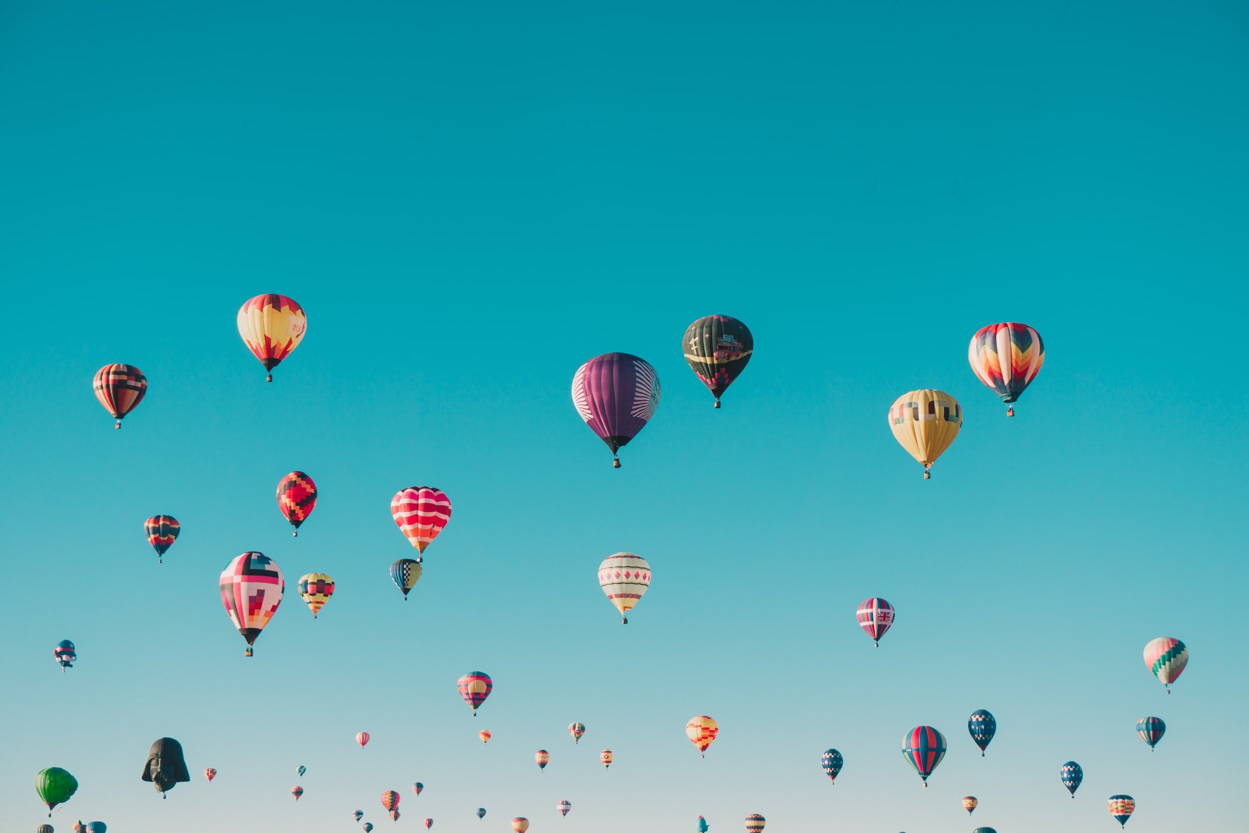 Numerous hot air balloons against a bright blue sky.