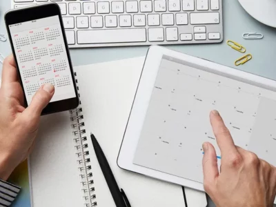 Person working at a desk using calendar apps on their phone and tablet.
