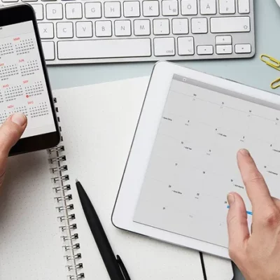 Person working at a desk using calendar apps on their phone and tablet.