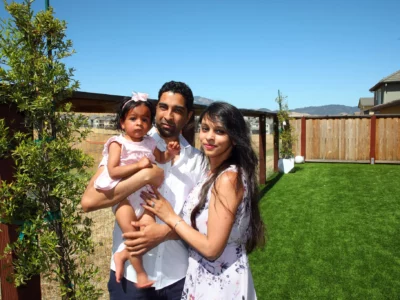 Young couple holding toddler while standing in their backyard.