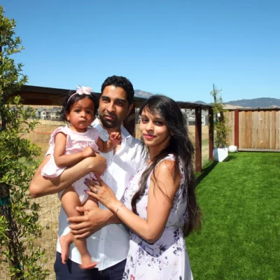 Young couple holding toddler while standing in their backyard.